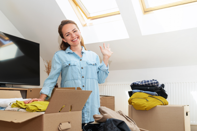 Woman unpacking her clothing smiling and waving hand. Moving house concept