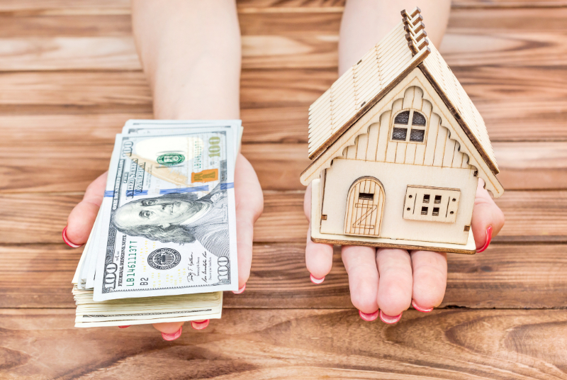 Woman's hands holding money and model of house over wooden table
